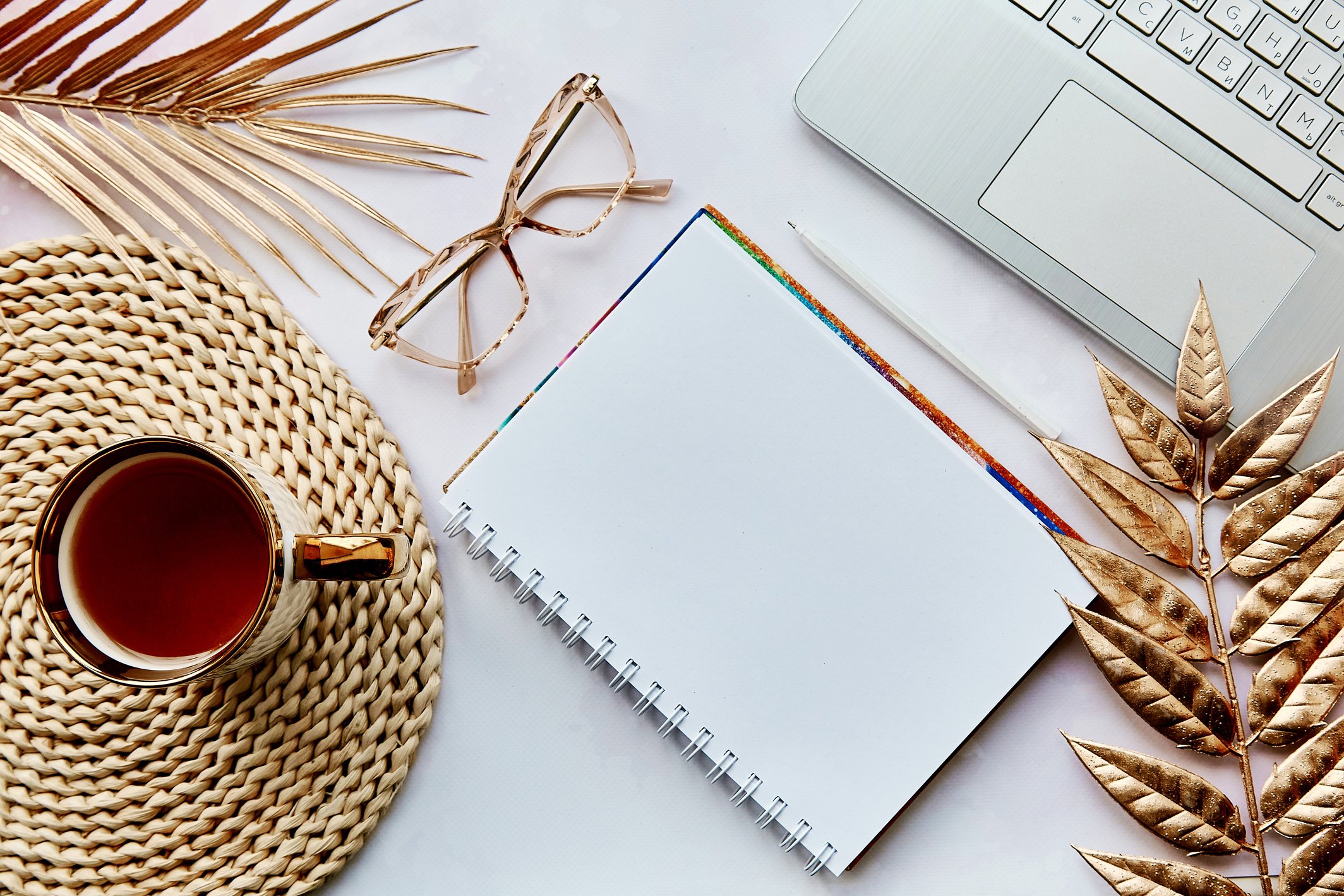 Golden aesthetic decorations with mock up notepad, laptop, tea cup and glasses. New year resolution, new start and list of goals concept. Cozy home. Top view. Copy space